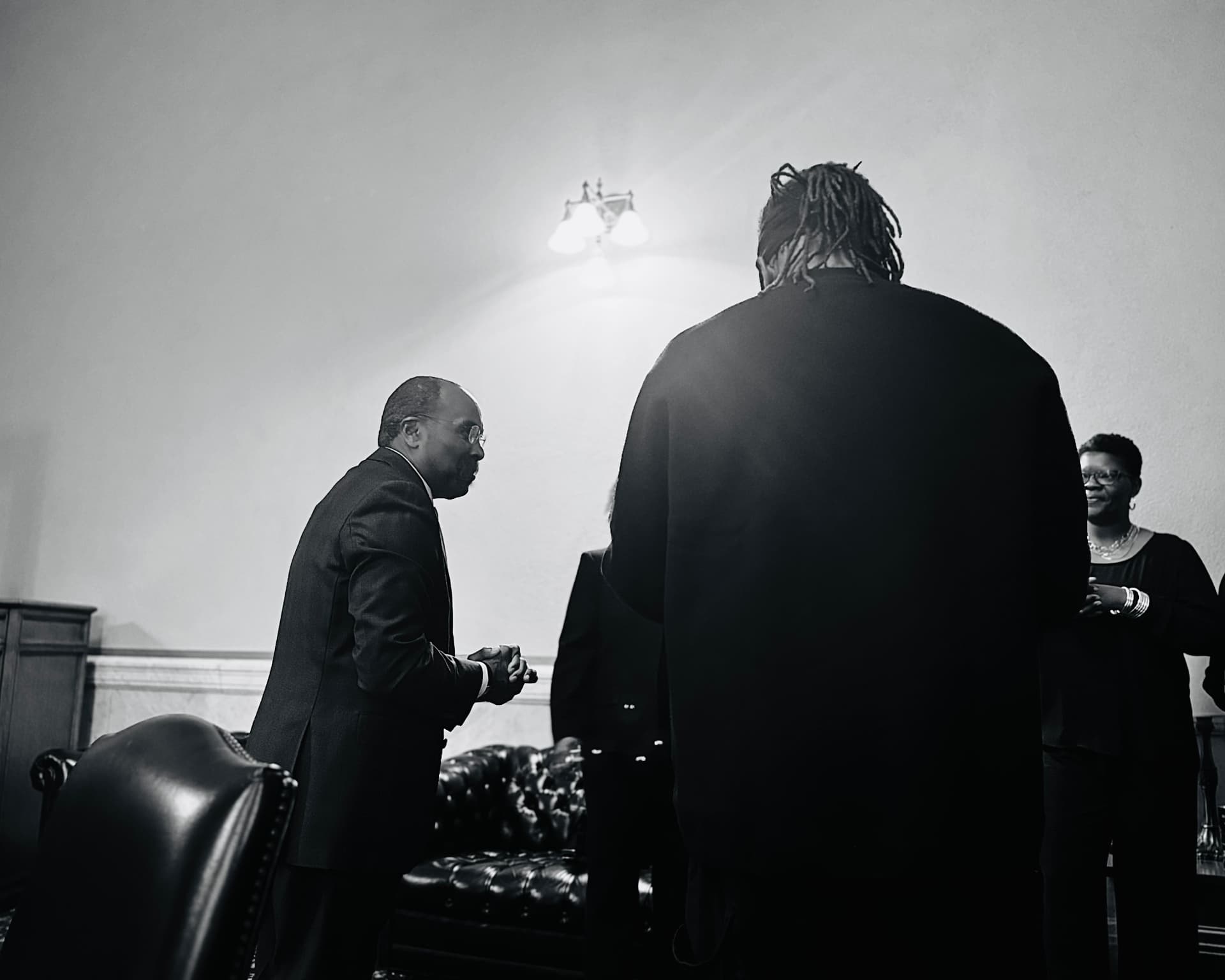 A man in a suit talking with a guest in a lounge with tufted black leather seating