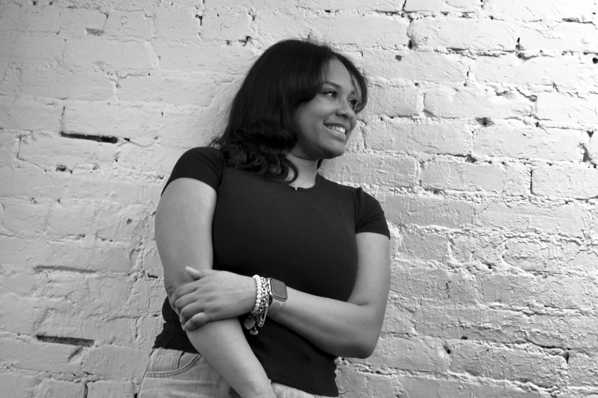 A smiling woman leaning against a white brick wall