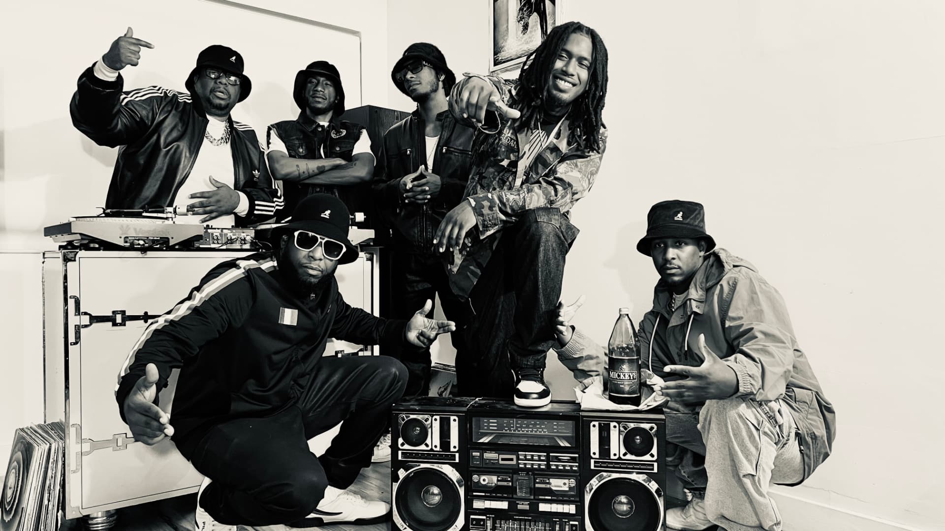 A group of seven men posing with boomboxes, turntables and vinyl records