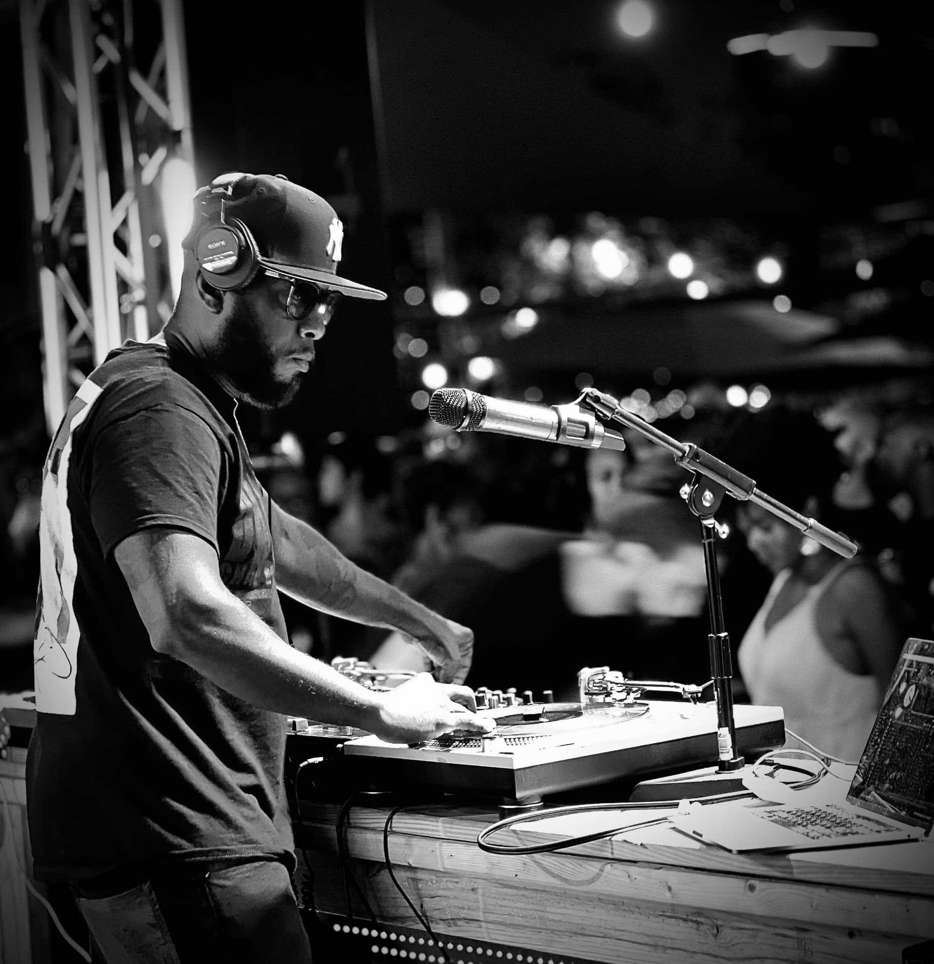 A DJ at the turntables with a microphone and a crowd behind him