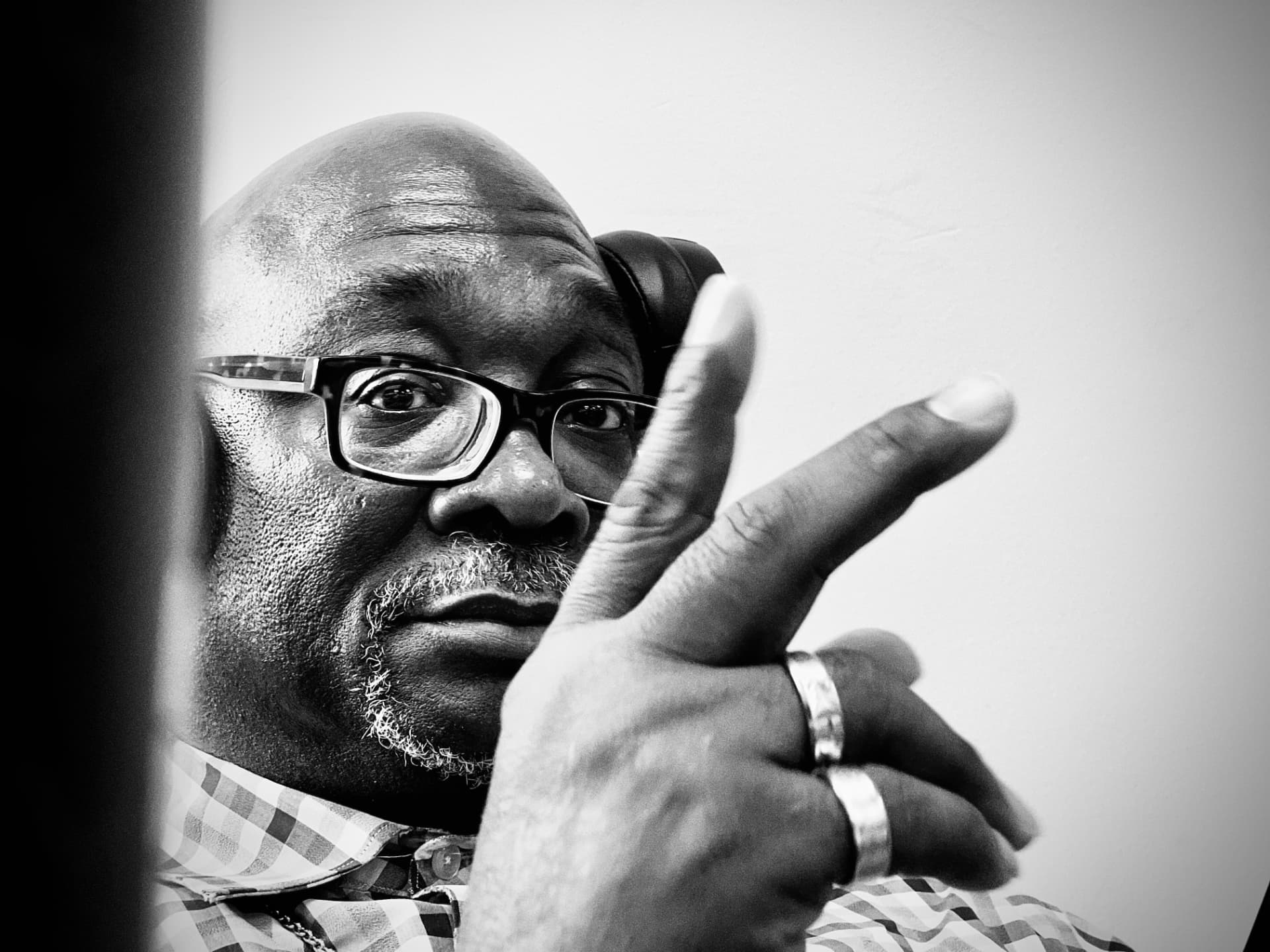 A close-up portrait of a man with glasses making a peace sign